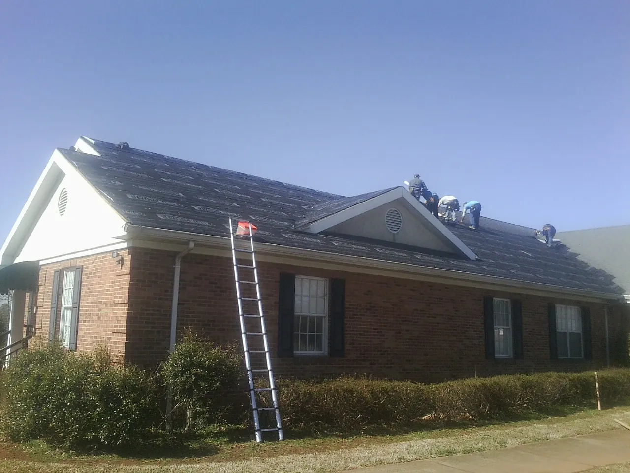 Crew tearing shingles off a brick ranch roof with a ladder set — Metal Roof Repair work by our crew in Tippecanoe