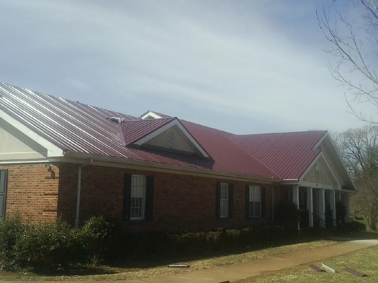 Red metal roof with gabled entries on a long brick building, from a Hail Damage Roof Repair job in Tippecanoe
