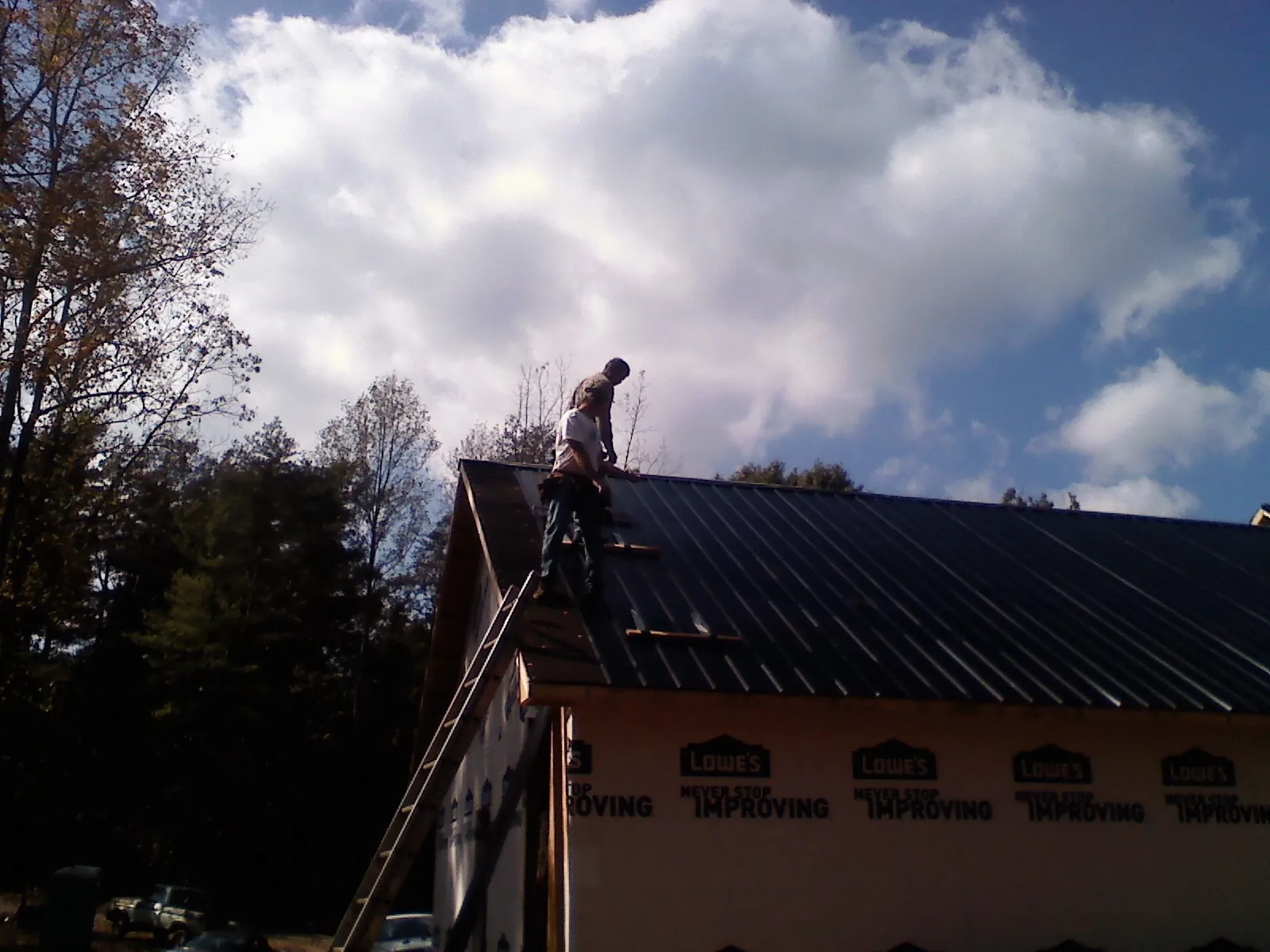 Roofer fastening dark metal panels high against a cloudy sky, from a Roof Inspection job in Tippecanoe