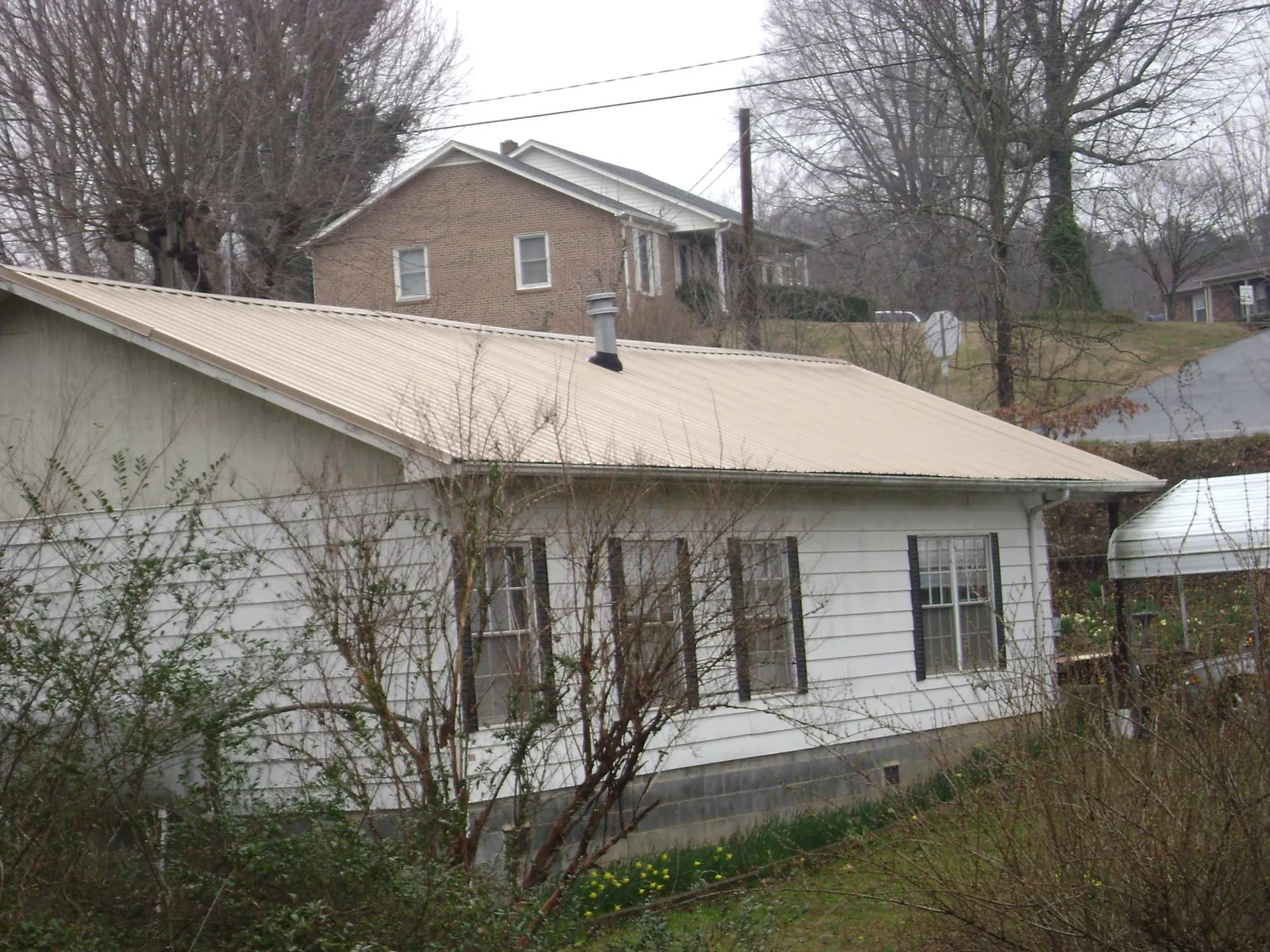 Tan metal roof on a white sided house set into a hillside — Commercial Roofing by Roofing Brothers in Tippecanoe
