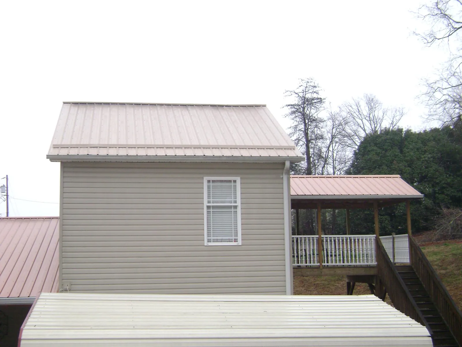 Tan metal roofs on a two story addition and attached porch, from a Roof Replacement job in Tippecanoe